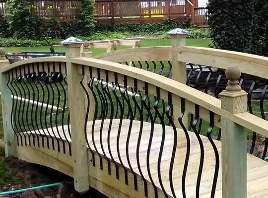 Curved wooden footbridge with black iron balusters